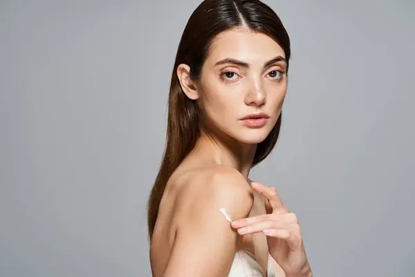 Una joven caucásica con crema en el hombro posa elegantemente, exudando elegancia y equilibrio. - foto de stock