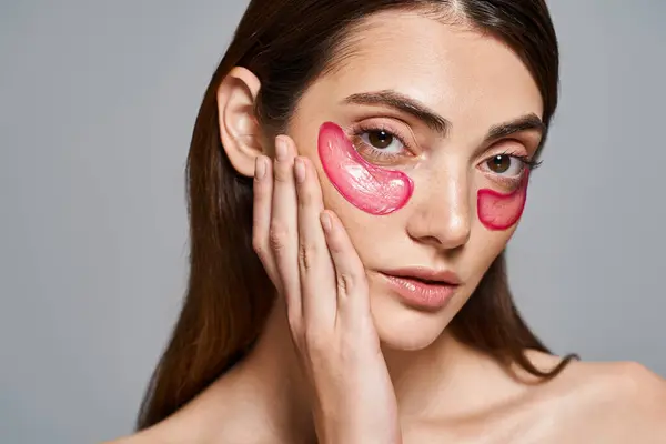 Une jeune femme caucasienne aux cheveux bruns portant des patchs roses vibrants sur son visage, créant un look audacieux et artistique. — Photo de stock