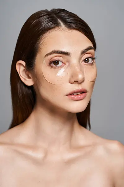 Une jeune femme caucasienne aux cheveux bruns et à la peau propre, présentant un patch sur sa joue. — Photo de stock