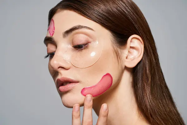 Una joven mujer caucásica con el pelo moreno tiene manchas de color rosa en la cara, creando un aspecto vibrante y artístico. - foto de stock