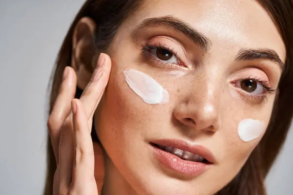 Молодая белая женщина с брюнетками и чистой кожей наслаждается роскошной процедурой для лица с большим количеством крема на лице. — стоковое фото