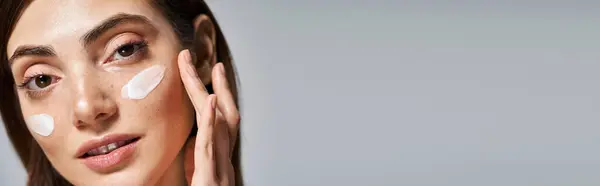 Молода кавказька жінка з брюнеткою посміхається з кремом на обличчі, банер — стокове фото