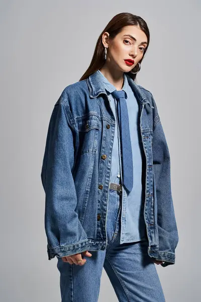 A young Caucasian woman with brunette hair and red lips stylishly wearing a denim jacket and jeans in a studio setting. — Stock Photo