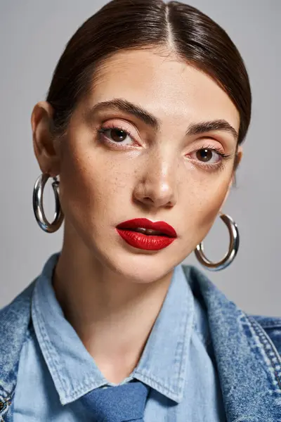Una joven mujer caucásica luciendo lápiz labial rojo y grandes pendientes de aro en un entorno de estudio. - foto de stock