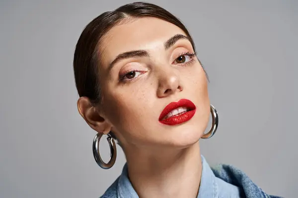 Uma jovem mulher caucasiana com cabelo morena e pele limpa vestindo grandes brincos de argola e batom vermelho arrojado. — Fotografia de Stock