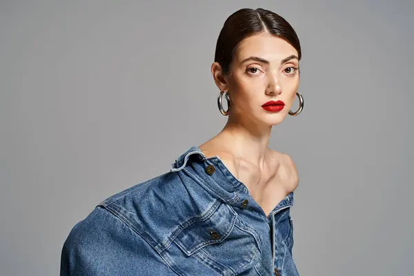 Une jeune femme caucasienne aux cheveux bruns et à la peau propre déchire une chemise en denim assortie d'un rouge à lèvres rouge audacieux. — Photo de stock