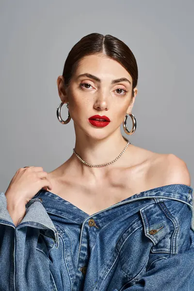 Uma jovem mulher caucasiana elegante com cabelo morena mostra seu estilo ousado em uma jaqueta jean e batom vermelho impressionante. — Fotografia de Stock