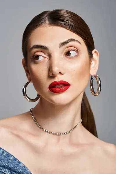 Una giovane donna caucasica elegante in uno studio, indossa rossetto rosso e grandi orecchini a cerchio, trasudando fiducia e raffinatezza. — Foto stock