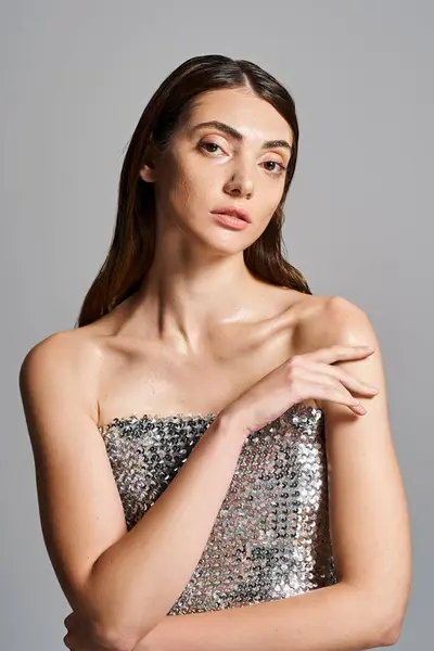 A young Caucasian woman with brunette hair poses in a stunning silver dress, exuding elegance and confidence. — Stock Photo