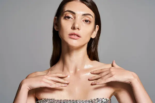 A young Caucasian woman with brunette hair wearing a strapless dress holds her hands on her chest in a studio setting. — Stock Photo