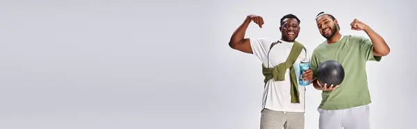 Sport banner, happy african american male friends holding ball and water bottle on grey backdrop — Stock Photo