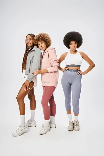 Pretty african american female friends in sportswear looking at camera on grey backdrop, Juneteenth — Stock Photo