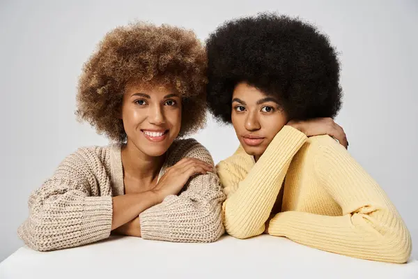 Кучеряві і щасливі афроамериканські друзі, що стоять в елегантному вбранні на сірому фоні, жовтень — стокове фото