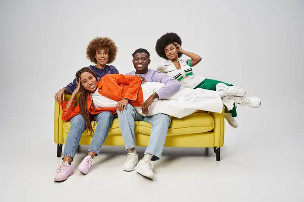 Cheerful african american woman with dreadlocks lying on laps of friends sitting on yellow couch — Stock Photo