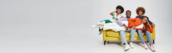 Happy african american woman with dreadlocks lying on laps of friends on yellow couch, banner — Stock Photo