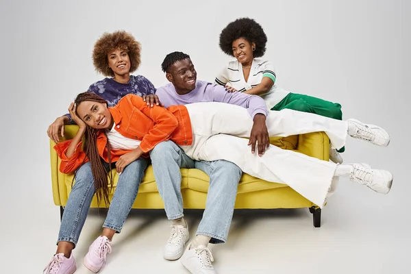 Sorrindo mulher afro-americana com dreadlocks deitado em voltas de amigos sentados no sofá amarelo — Fotografia de Stock