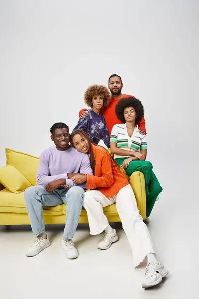 Joyeux amis afro-américains en tenue décontractée colorée assis ensemble sur le canapé jaune sur gris — Photo de stock