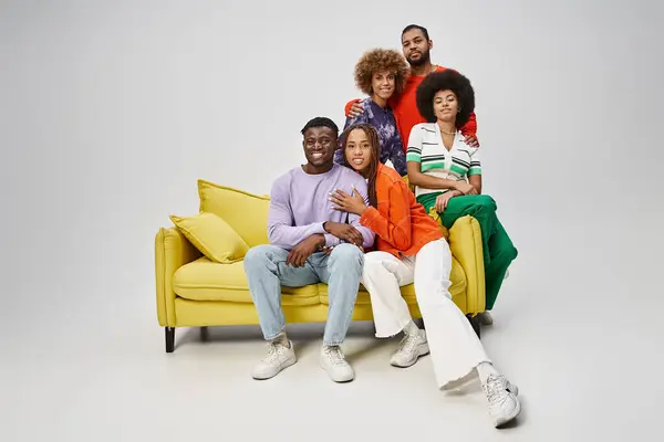 Happy african american people in bright casual wear sitting together on yellow couch on grey — Stock Photo