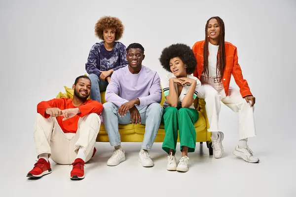 Cheerful african american people in bright casual wear sitting together on yellow couch on grey — Stock Photo