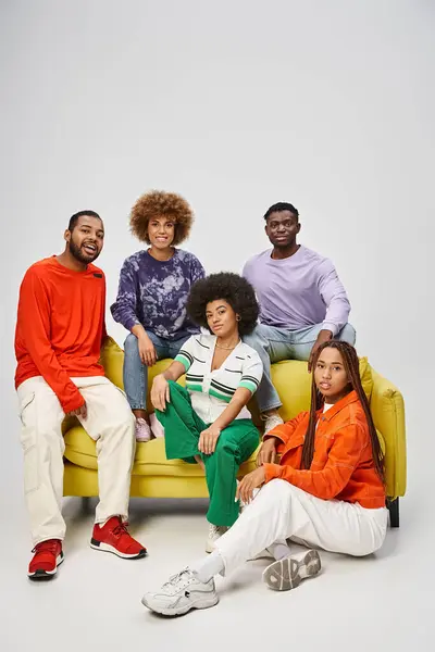 Positive african american people in bright casual wear sitting together on yellow couch on grey — Stock Photo