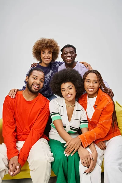 Joyful african american community in bright casual wear sitting together on yellow couch on grey — Stock Photo