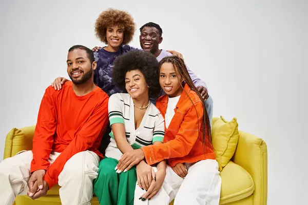 Cheerful african american community in colorful casual wear sitting together on yellow couch on grey — Stock Photo
