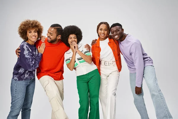 Fröhliche afrikanisch-amerikanische Menschen in bunten Freizeitanzügen lachen gemeinsam auf grauem Hintergrund — Stockfoto