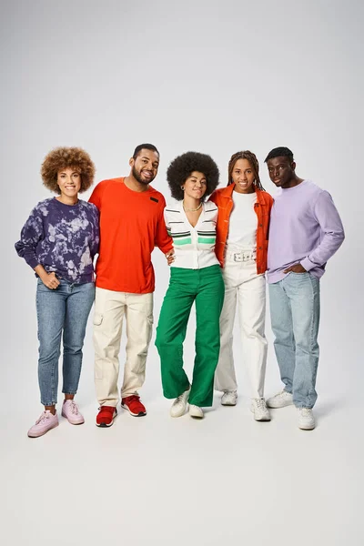 Happy african american woman hugging her friends in vibrant attire on grey background, Juneteenth — Stock Photo
