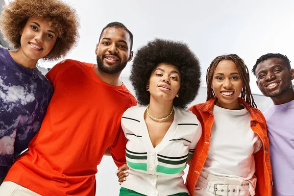 Joyful african american woman hugging her friends in vibrant attire on grey background, Juneteenth — Stock Photo