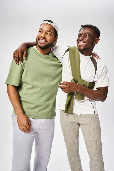 Positive african american male friends in casual wear hugging on grey background, Juneteenth — Stock Photo