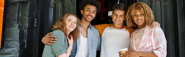 Smiling and stylish multiethnic students embracing near campus on city street, horizontal banner — Stock Photo