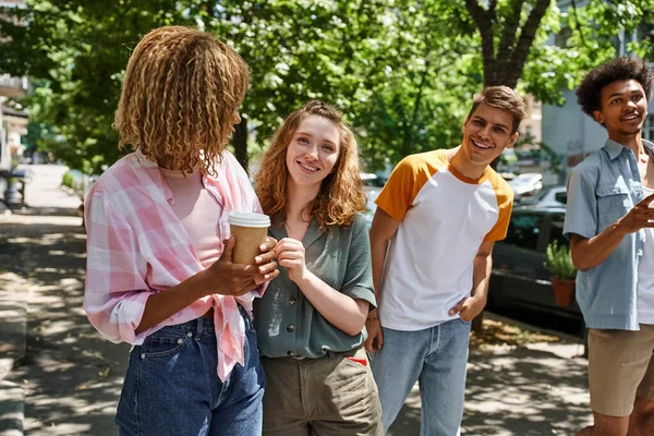 Cheerful and fashionable multiethnic students walking on city in modern city, traveling friends — Stock Photo