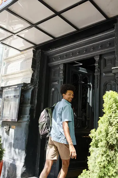 Joyful and trendy african american student with backpack entering youth hotel on city street — Stock Photo