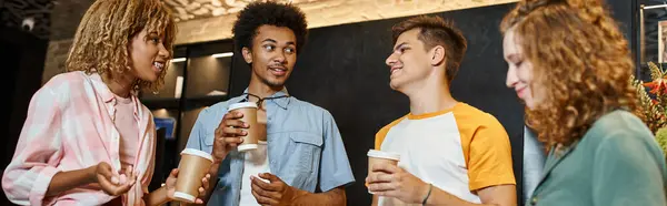 Copains multiculturels souriants et branchés avec des tasses en papier parlant dans le hall de l'auberge de jeunesse, bannière — Photo de stock