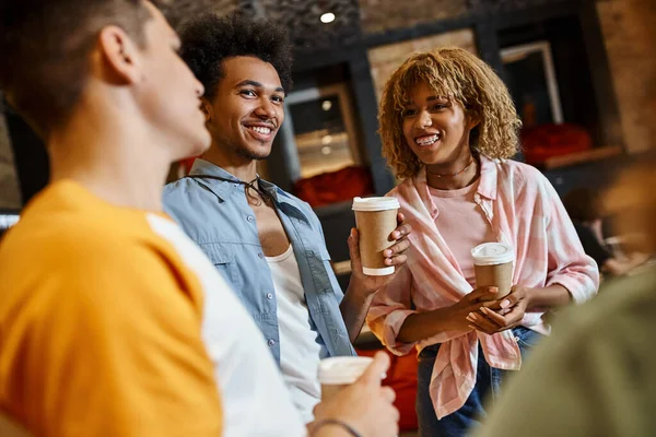 Cheerful multicultural buddies with paper cups talking in lobby of hostel, travel and friendship — Stock Photo