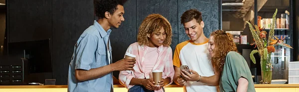 Cara sorridente mostrando smartphone para amigos multiétnicos com copos de papel no lobby do albergue, banner — Fotografia de Stock