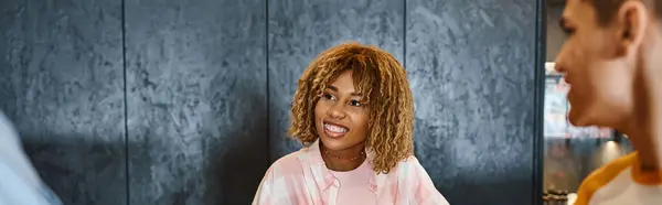 Jovem e elegante afro-americano recepcionista sorrindo perto de estudantes em albergue da juventude, bandeira — Fotografia de Stock