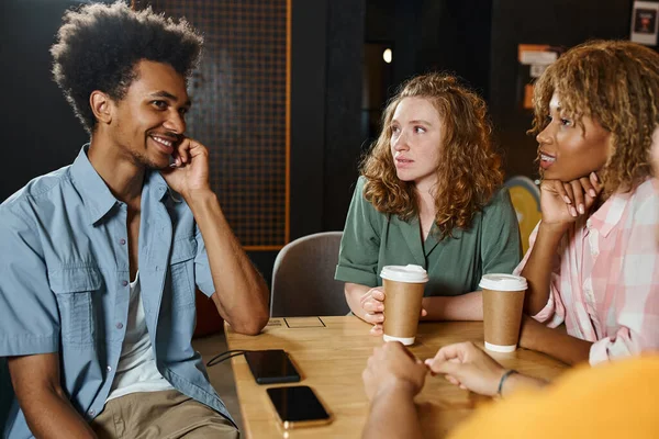 Smiling and stylish african american man talking to multicultural friends in cafe of students hostel — Stock Photo