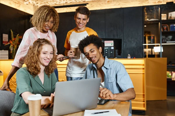 Joyful multiethnic buddies looking at laptop in lounge cafe of students hostel, learning and travel — Stock Photo
