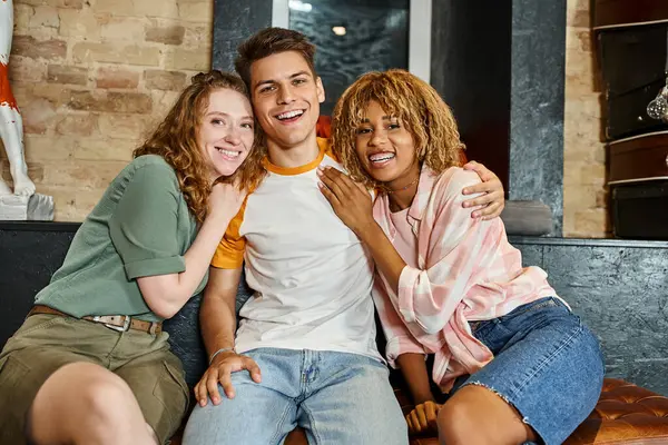 Étudiants multiculturels excités et élégants embrasser et regarder la caméra dans le salon de l'auberge de jeunesse — Photo de stock