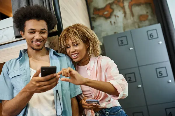Joyful african american couple looking at smartphone in cozy room of students hostel, roommates — Stock Photo