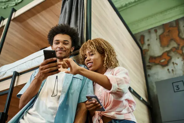 Low-Winkelansicht eines jungen afrikanisch-amerikanischen Paares, das im Zimmer eines Studentenwohnheims auf sein Smartphone schaut — Stockfoto