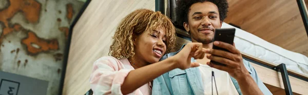 Low angle view of african american students looking at smartphone in room of youth hostel, banner — Stock Photo