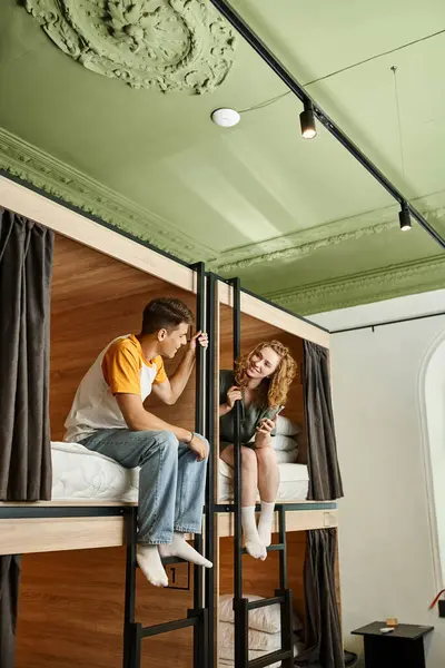 Щаслива пара студентів розмовляє на двоспальних ліжках в затишному номері сучасних студентів гуртожиток, мандрівників — стокове фото