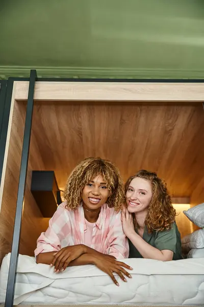 Heureux multiculturels amis féminins couché sur un lit double étage confortable et regardant la caméra dans l'auberge — Photo de stock