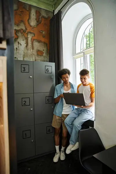 Jóvenes estudiantes interracial mirando portátil cerca de casillero en la habitación del albergue juvenil, viajeros - foto de stock