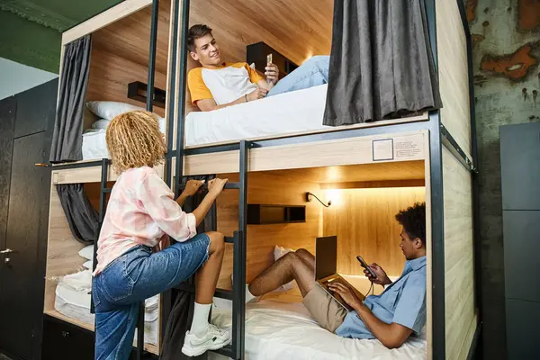 African american woman near multiethnic buddies with digital devices on double-decker bed in hostel — Stock Photo