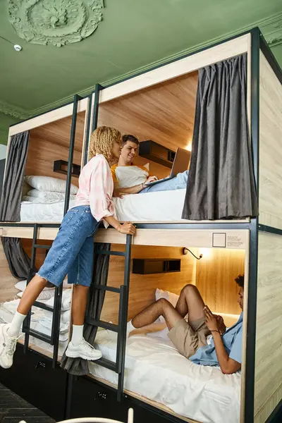 African american woman near multiethnic friends using gadgets on double-decker bed in hostel — Stock Photo