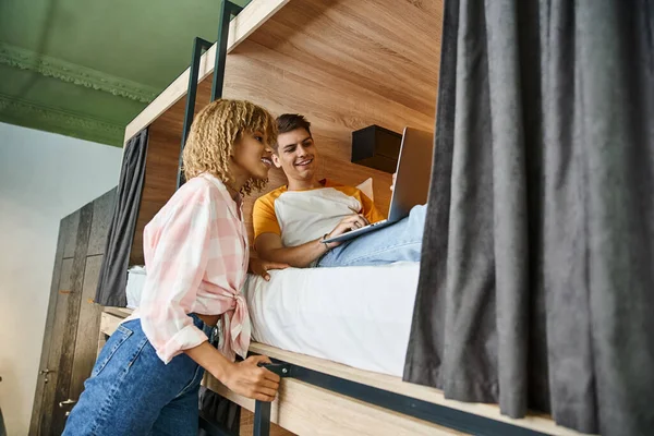 Cheerful african american woman near friend using laptop on double-decker bed in students hostel — Stock Photo