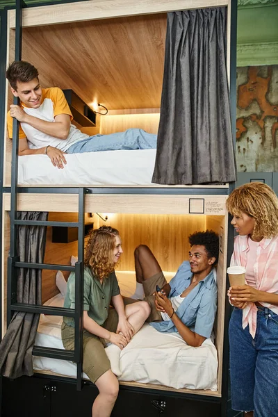 Cheerful multicultural students talking on double-decker bed in cozy hostel room, travelers — Stock Photo